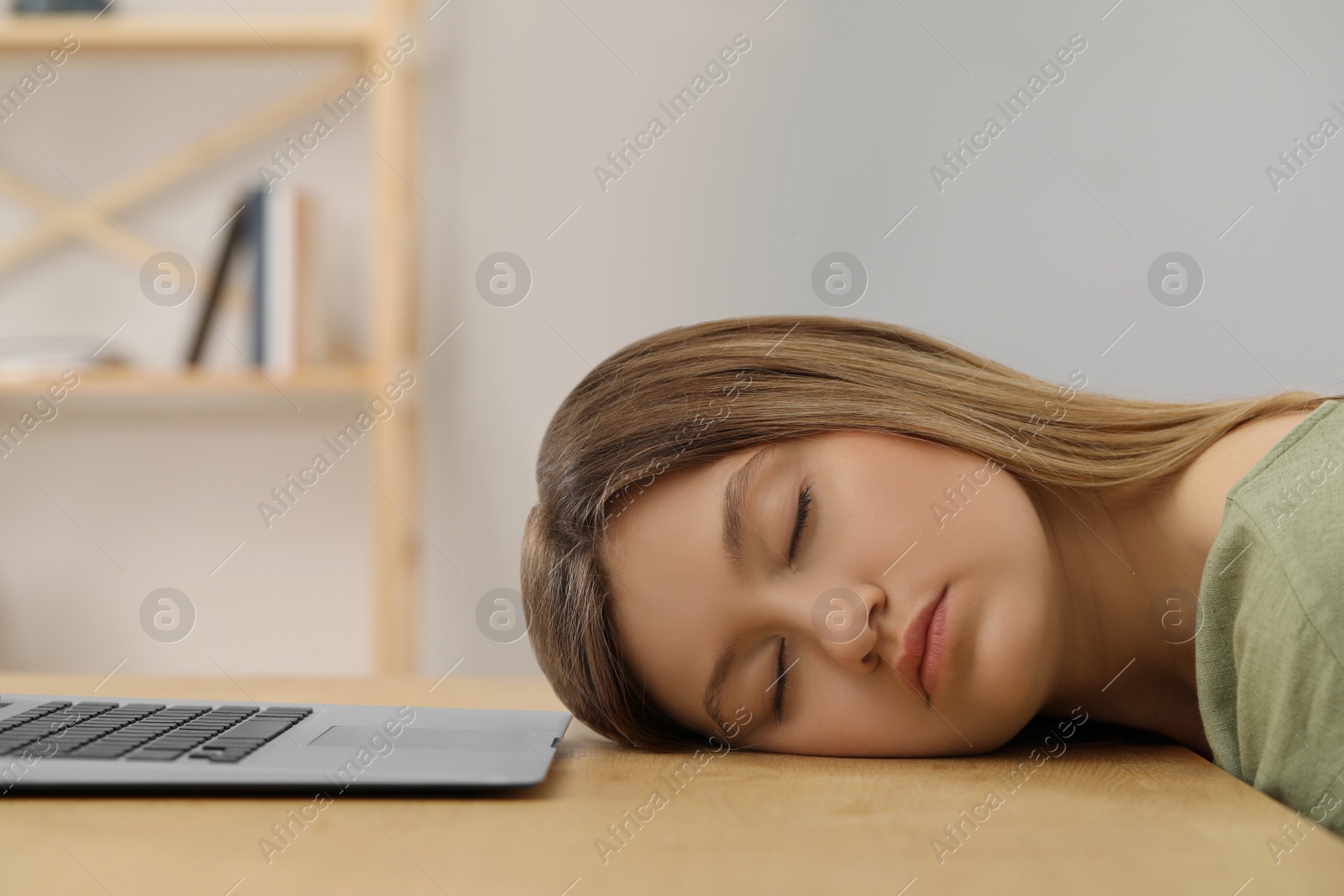 Photo of Young woman sleeping in front of laptop at wooden table indoors