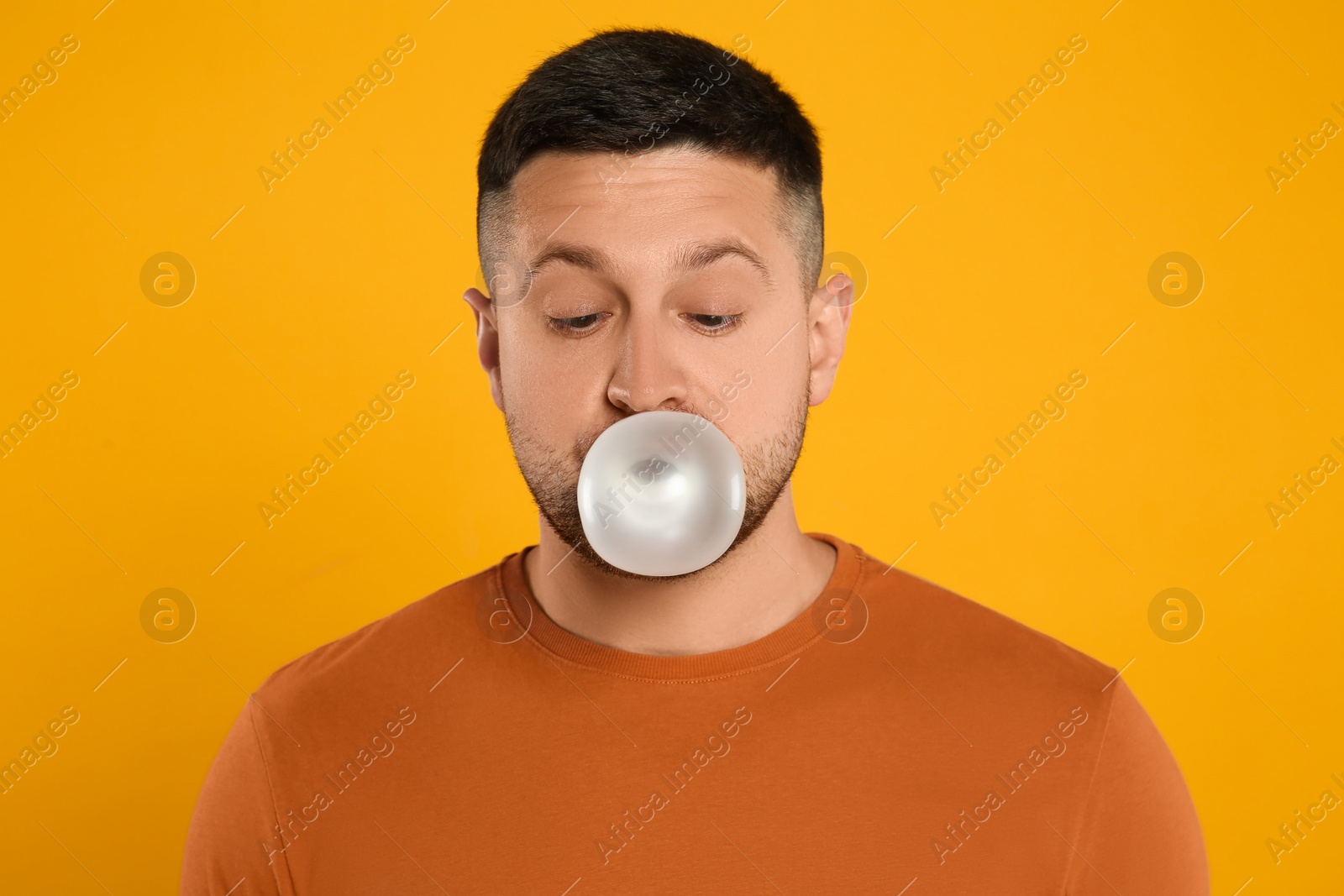 Photo of Handsome man blowing bubble gum on orange background