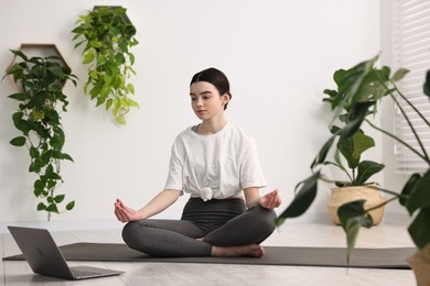 Beautiful girl meditating on mat near laptop in yoga studio