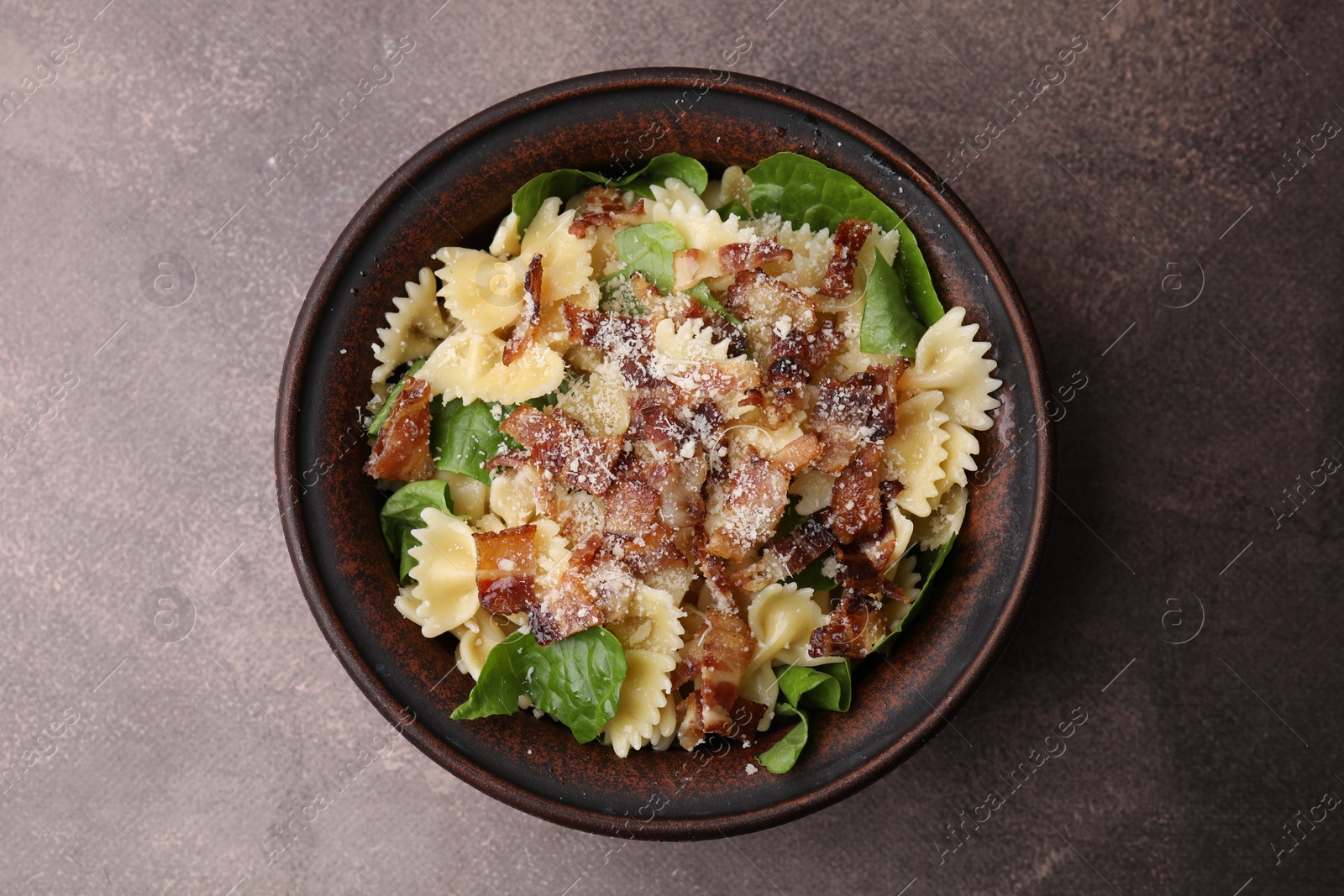 Photo of Tasty pasta with bacon and basil on brown table, top view