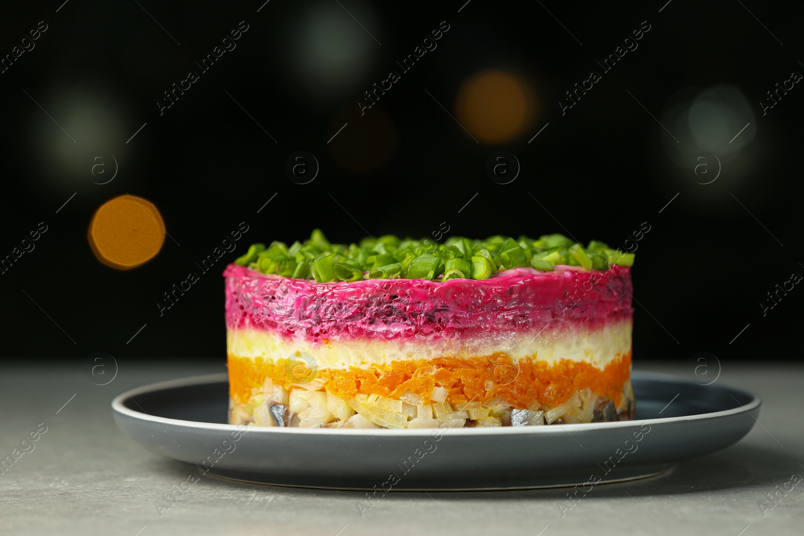 Photo of Herring under fur coat salad on grey table against blurred festive lights, closeup with space for text. Traditional Russian dish