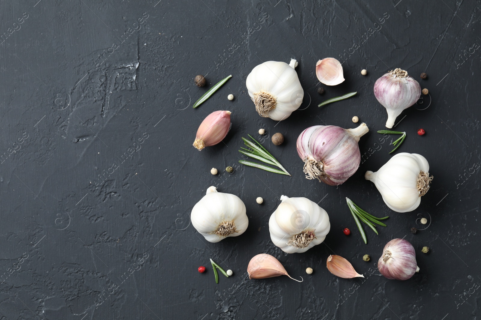 Photo of Fresh garlic, rosemary and peppercorns on dark textured table, flat lay. Space for text