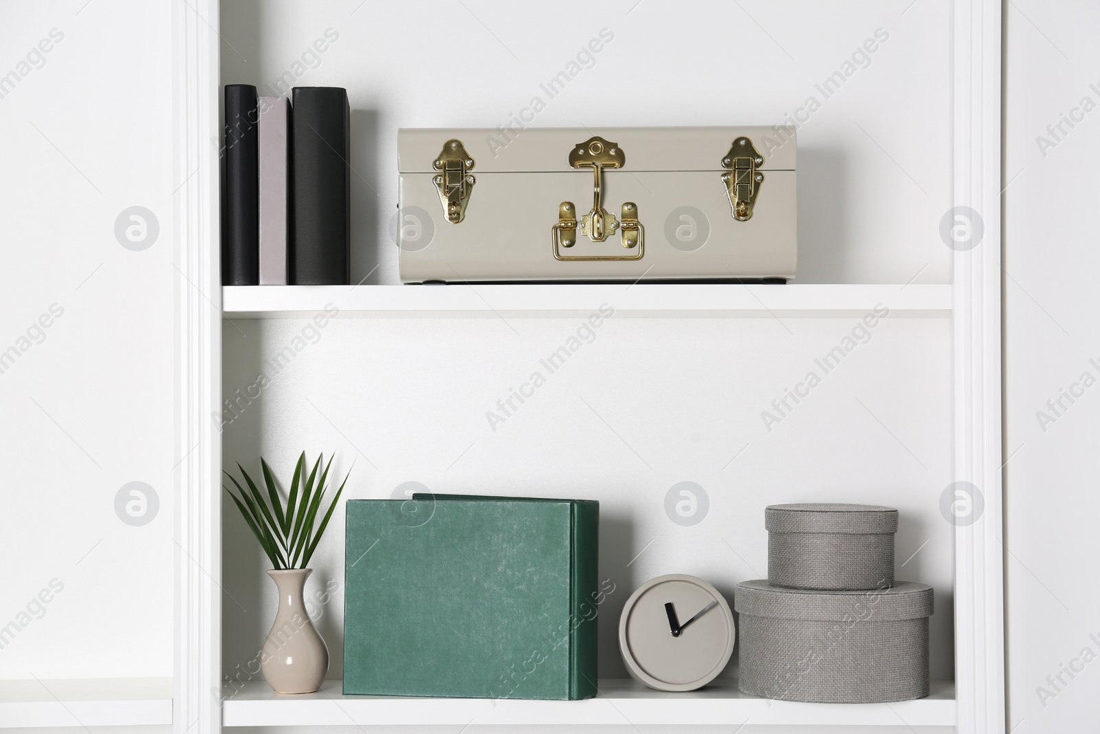 Photo of White shelves with clock, books and different decor indoors. Interior design