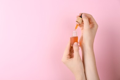 Photo of Woman holding bottle of essential oil on pink background, closeup. Space for text