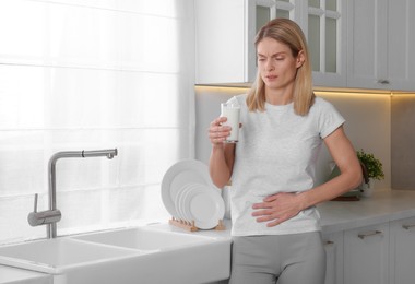 Photo of Woman with glass of milk suffering from lactose intolerance in kitchen, space for text