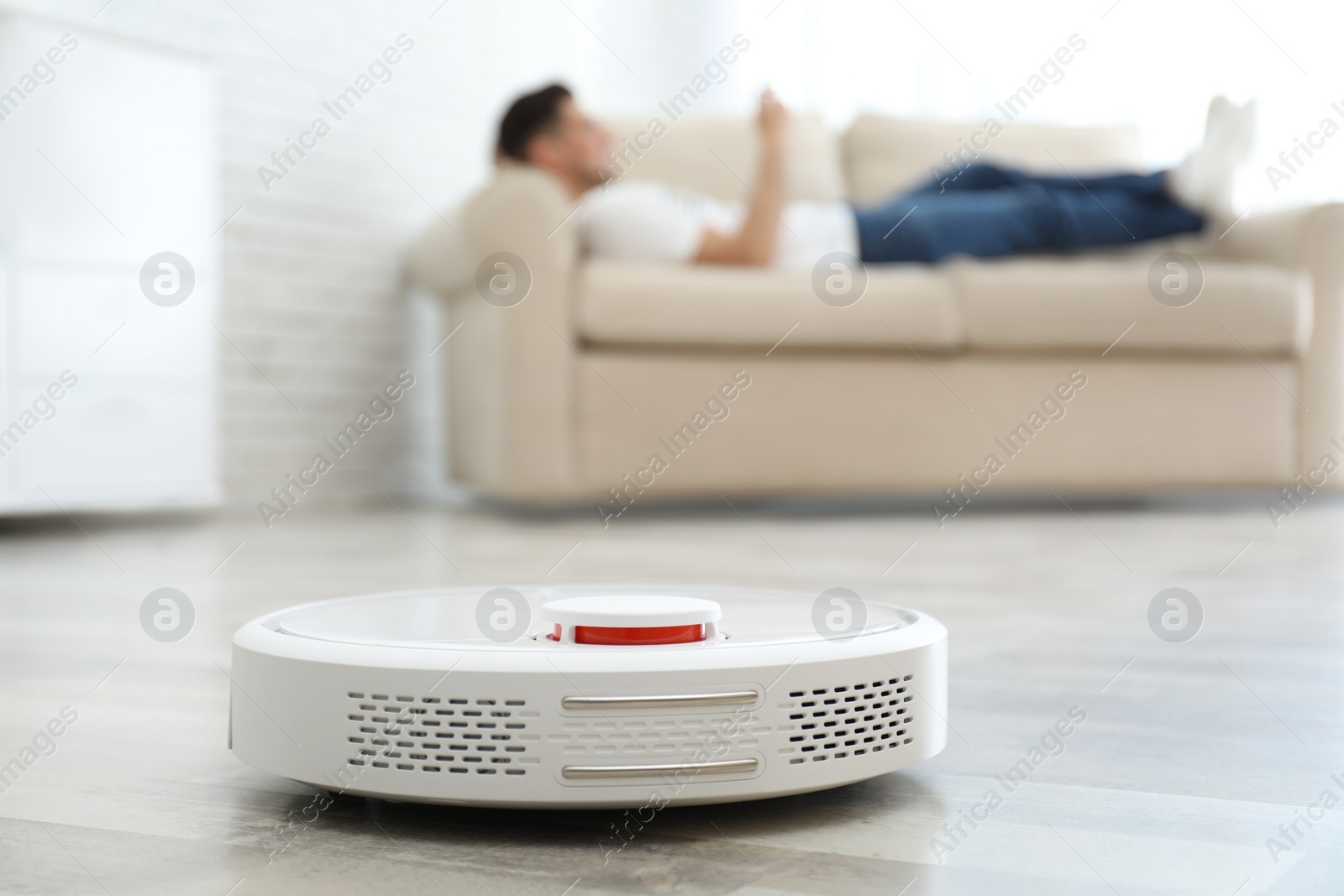 Photo of Man resting on sofa while robotic vacuum cleaner doing his work at home