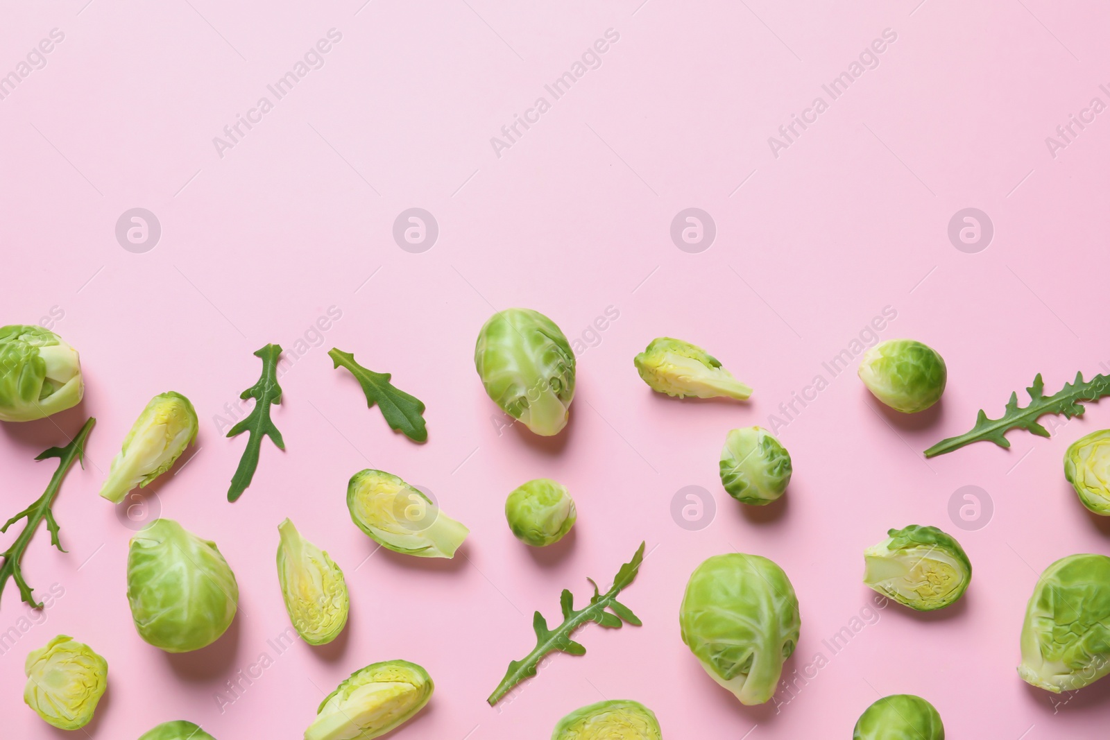 Photo of Fresh Brussels sprouts and arugula on color background, flat lay. Space for text