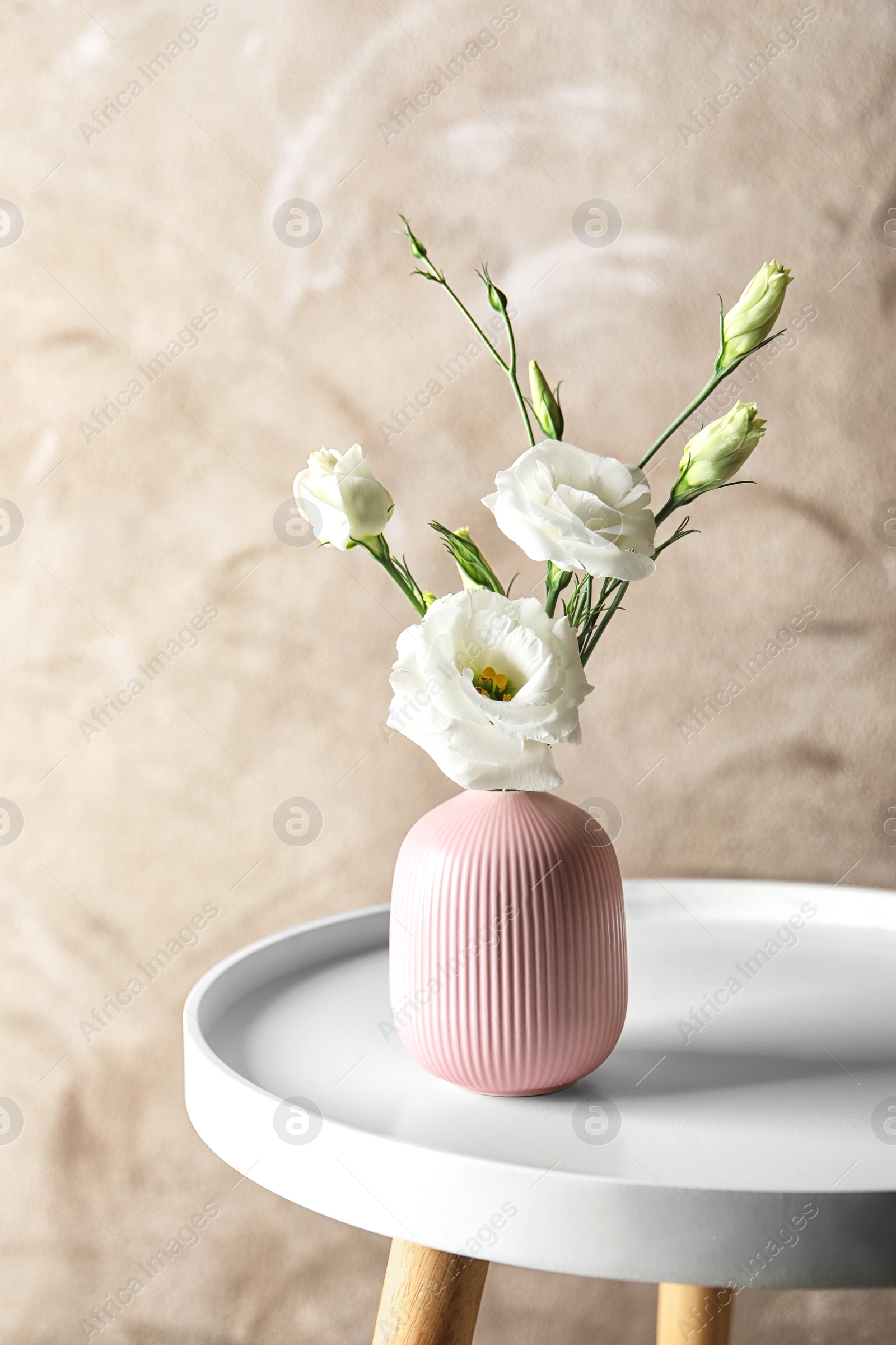 Photo of Vase with beautiful Eustoma flowers on table against color background