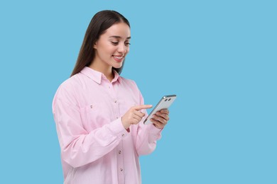Photo of Happy woman sending message via smartphone on light blue background, space for text