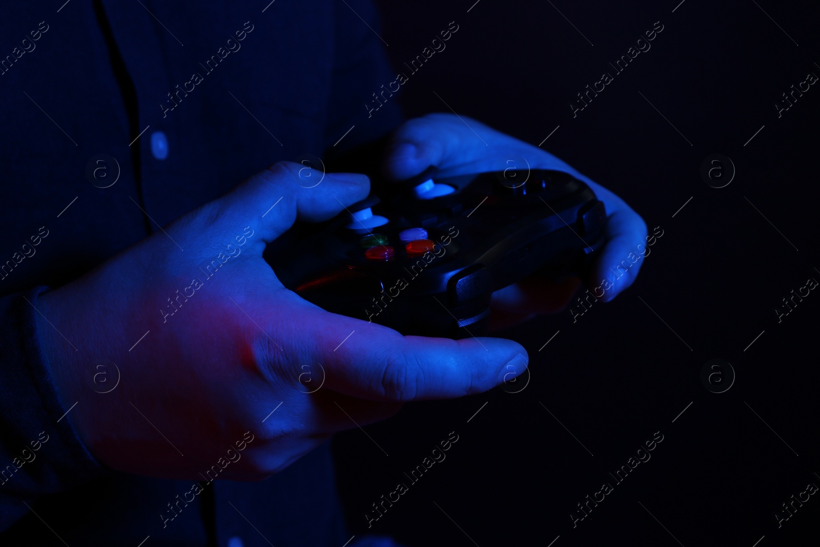 Photo of Man using wireless game controller on dark background in neon lights, closeup