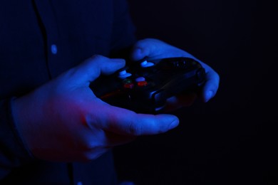 Man using wireless game controller on dark background in neon lights, closeup