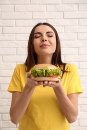 Young woman eating tasty burger near brick wall