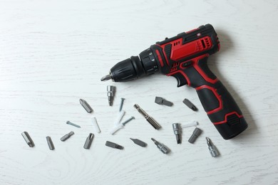 Photo of Electric screwdriver and different bits on white wooden table, flat lay