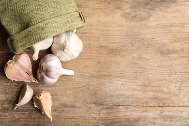 Photo of Fresh unpeeled garlic bulbs and sack on wooden table, flat lay with space for text. Organic product