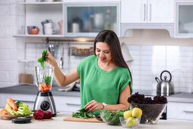 Photo of Young woman preparing tasty healthy smoothie at table in kitchen