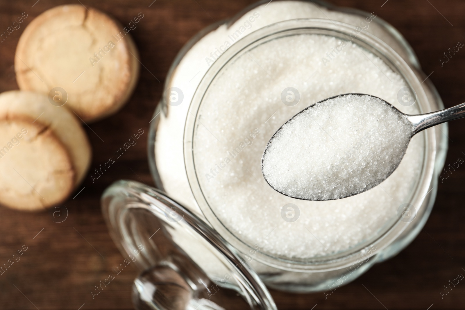 Photo of Taking spoon of sugar from glass bowl on wooden table, closeup