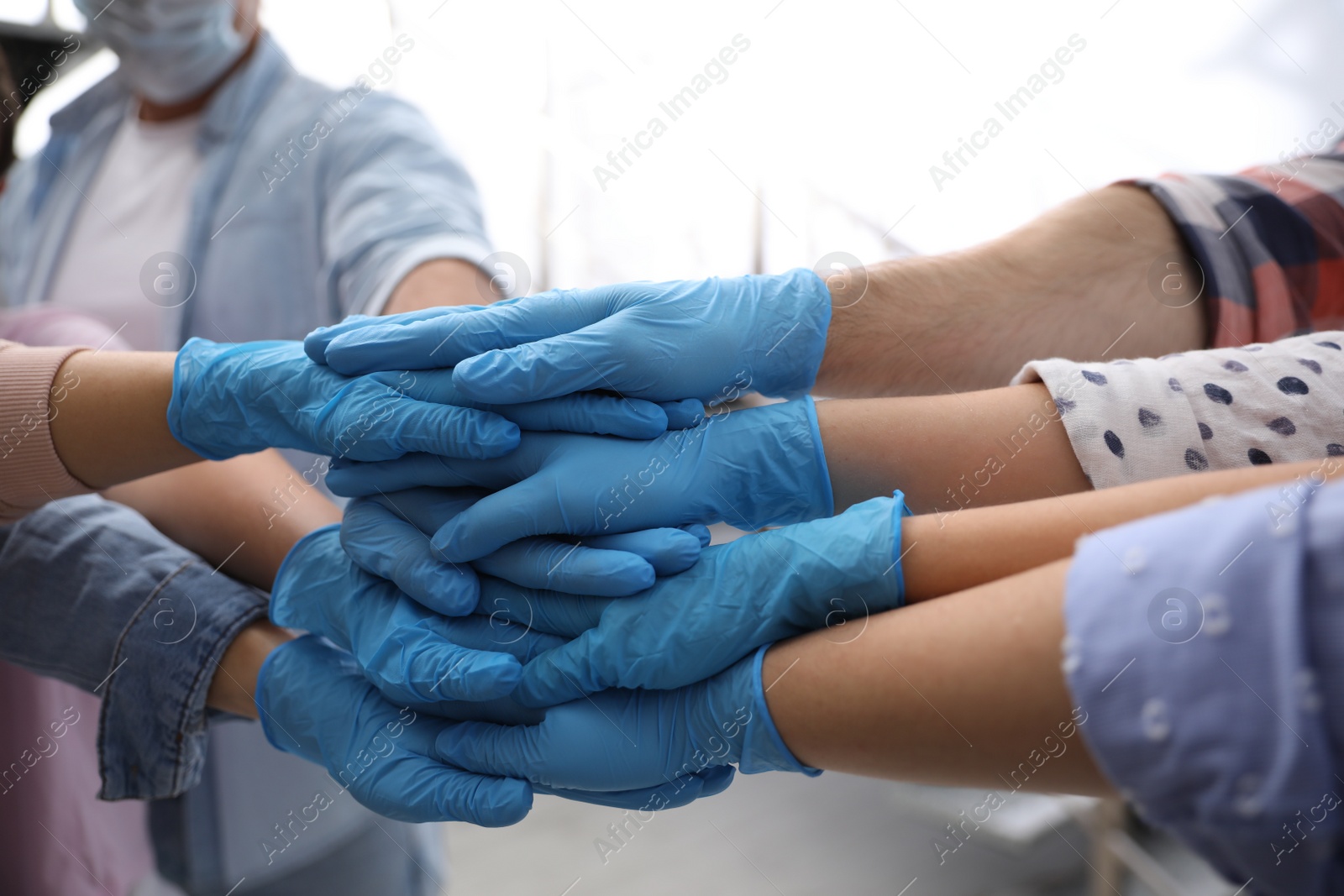 Photo of Group of people in blue medical gloves stacking hands indoors, closeup