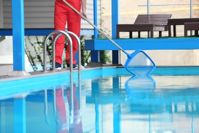 Photo of Male worker cleaning outdoor pool with scoop net