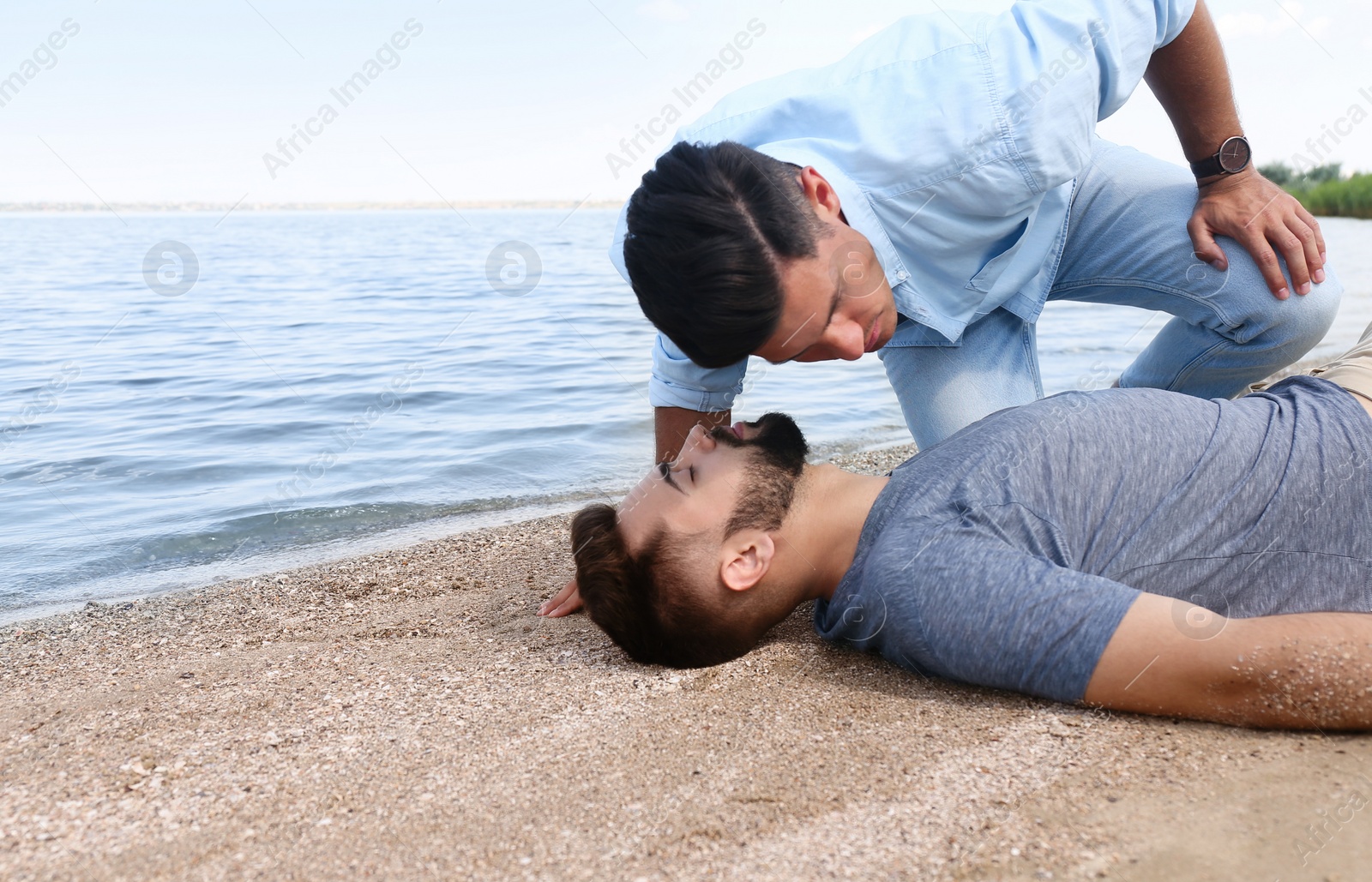 Photo of Passerby checking for breathing of unconscious young man near sea