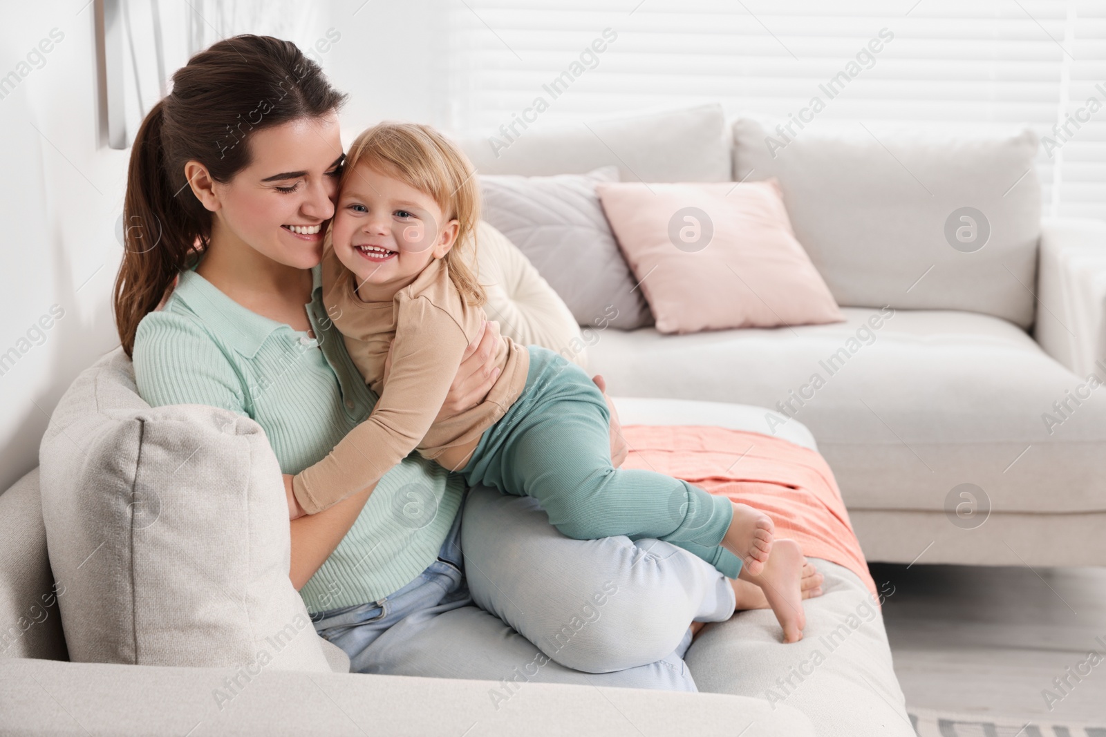 Photo of Mother with her cute little daughter on sofa at home, space for text