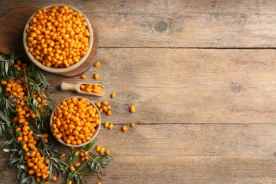 Photo of Ripe sea buckthorn berries on wooden table, flat lay. Space for text