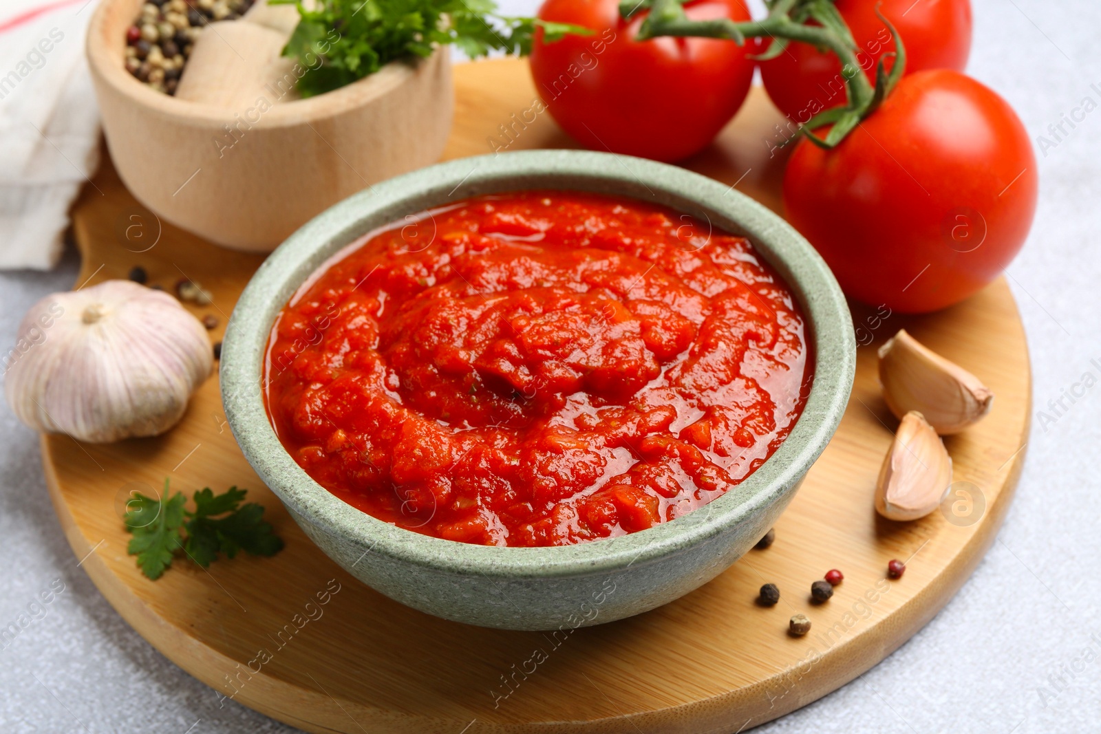 Photo of Homemade tomato sauce in bowl and fresh ingredients on light grey table, closeup