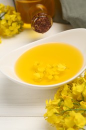 Rapeseed oil in gravy boat and beautiful yellow flowers on white wooden table