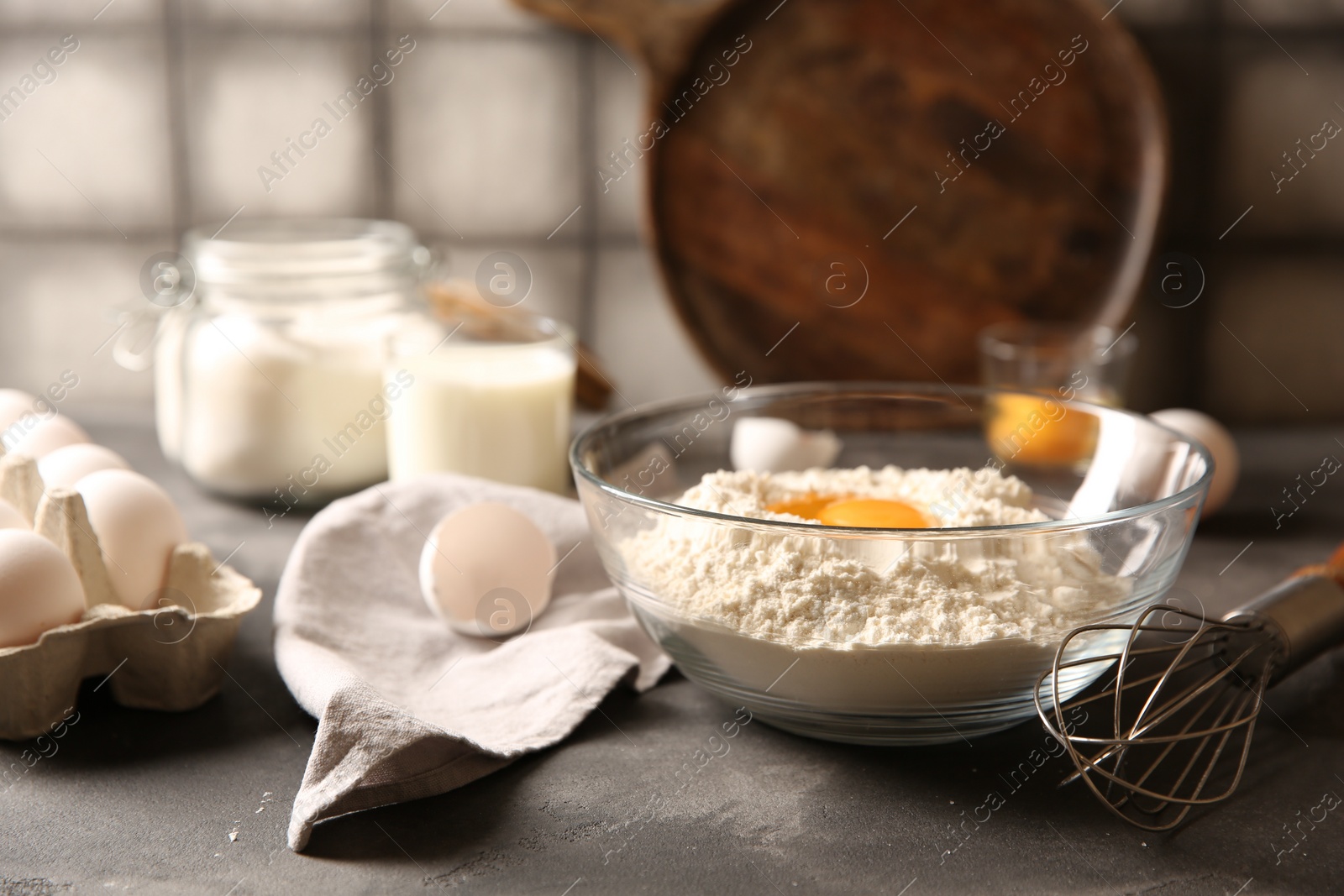 Photo of Making dough. Flour with egg yolk in bowl and whisk on grey textured table, closeup