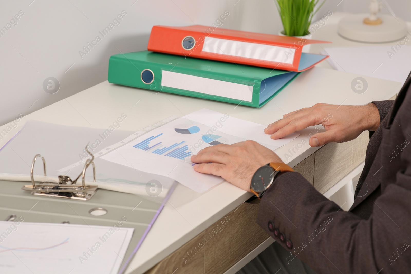 Photo of Businessman putting document into punched pocket at white table in office, closeup
