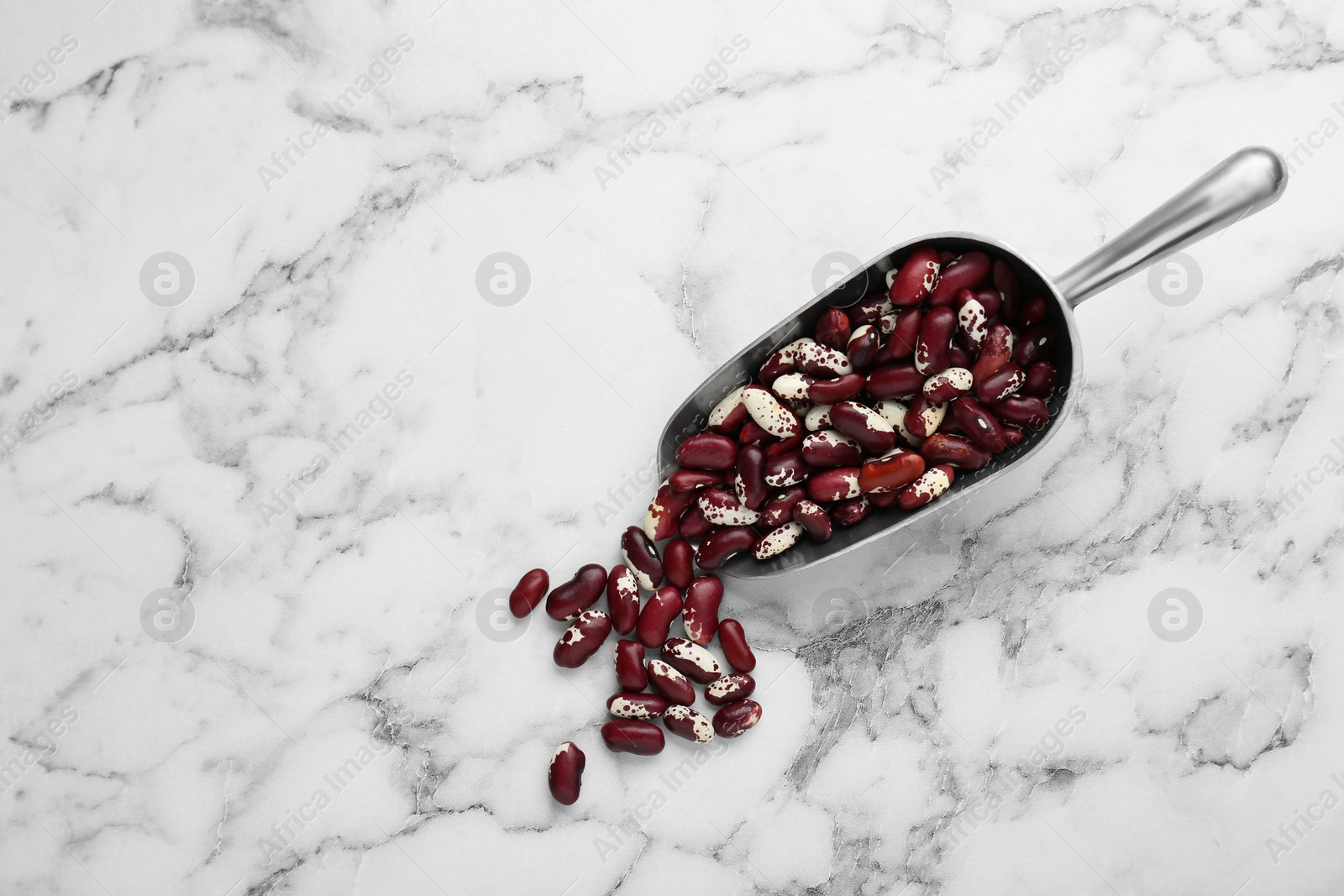 Photo of Metal scoop with dry kidney beans on white marble table, flat lay. Space for text