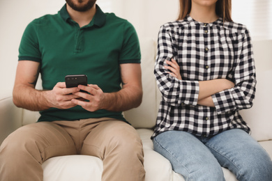 Photo of Young man preferring smartphone over his girlfriend at home, closeup. Relationship problems