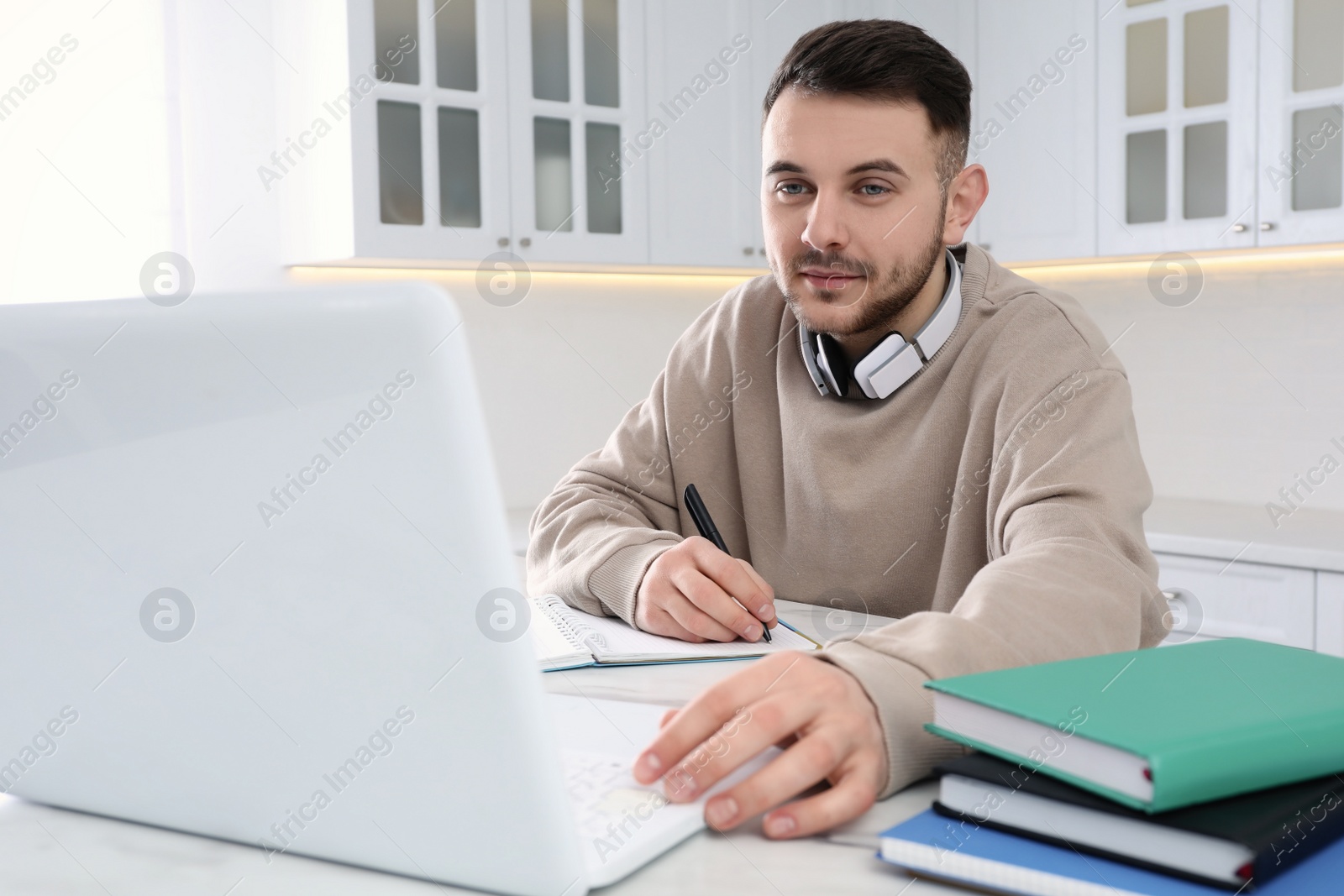 Photo of Young man using modern laptop for studying in kitchen. Distance learning