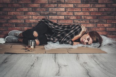 Image of Poor homeless woman sleeping on floor near brick wall