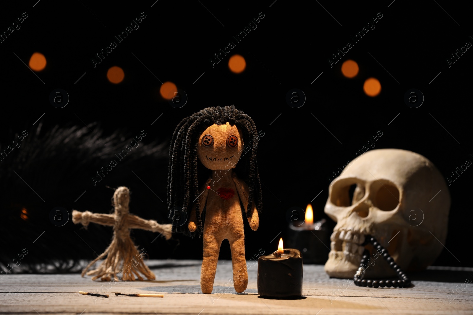 Photo of Female voodoo doll with pin in heart and ceremonial items on wooden table against blurred background