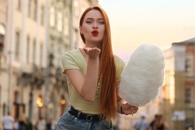 Beautiful woman with cotton candy blowing kiss on city street