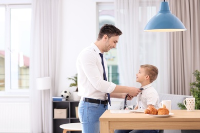 Photo of Dad helping his son knot necktie at home