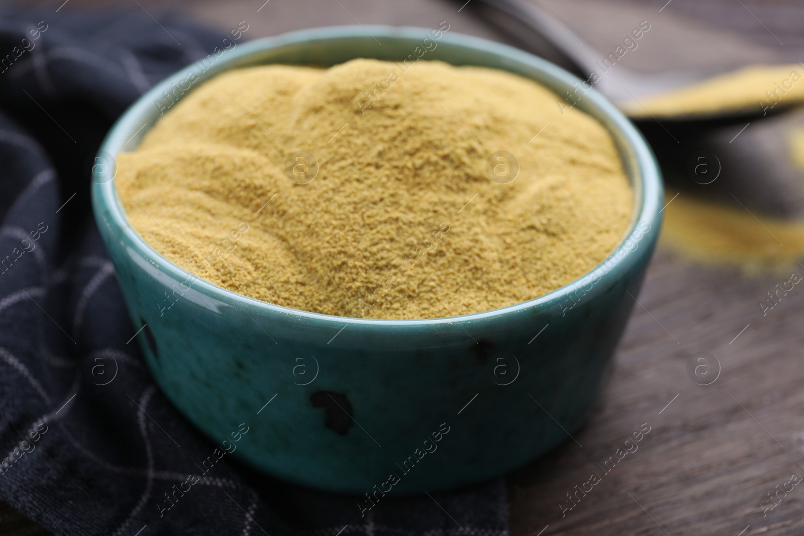 Photo of Granulated brewer`s yeast in bowl on wooden table, closeup