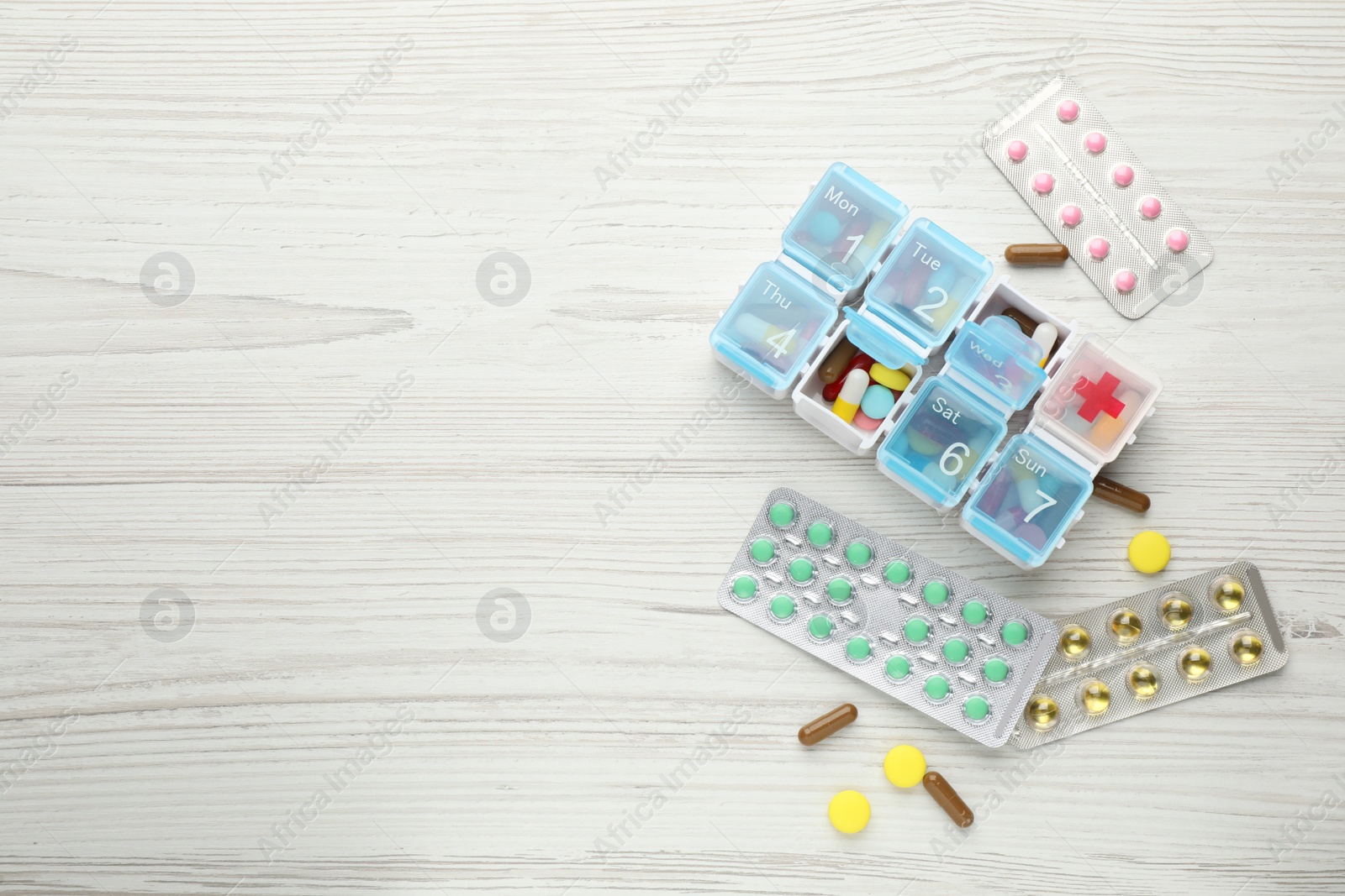Photo of Pill box with medicaments on white wooden table, flat lay. Space for text