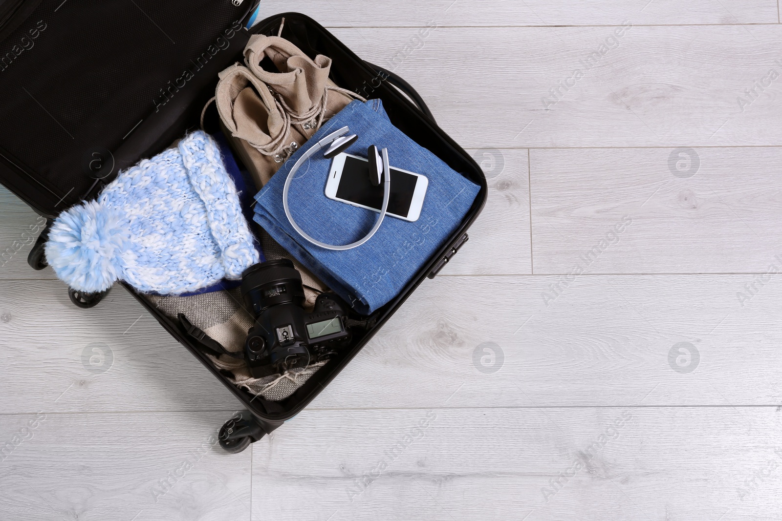 Photo of Open suitcase with warm clothes for winter vacation on wooden floor, top view. Space for text