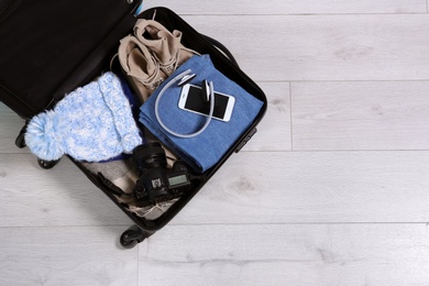 Open suitcase with warm clothes for winter vacation on wooden floor, top view. Space for text