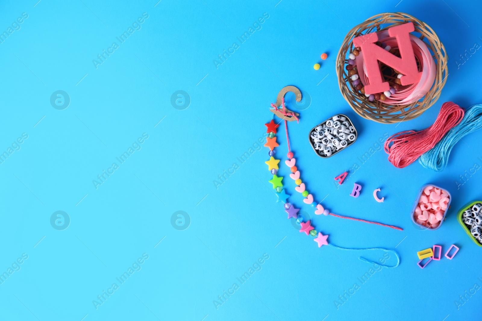 Photo of Kid`s handmade jewelry kit. Colorful beads, ribbon and bracelets on light blue background, flat lay. Space for text