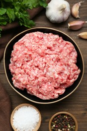 Bowl of raw fresh minced meat and ingredients on wooden table, flat lay