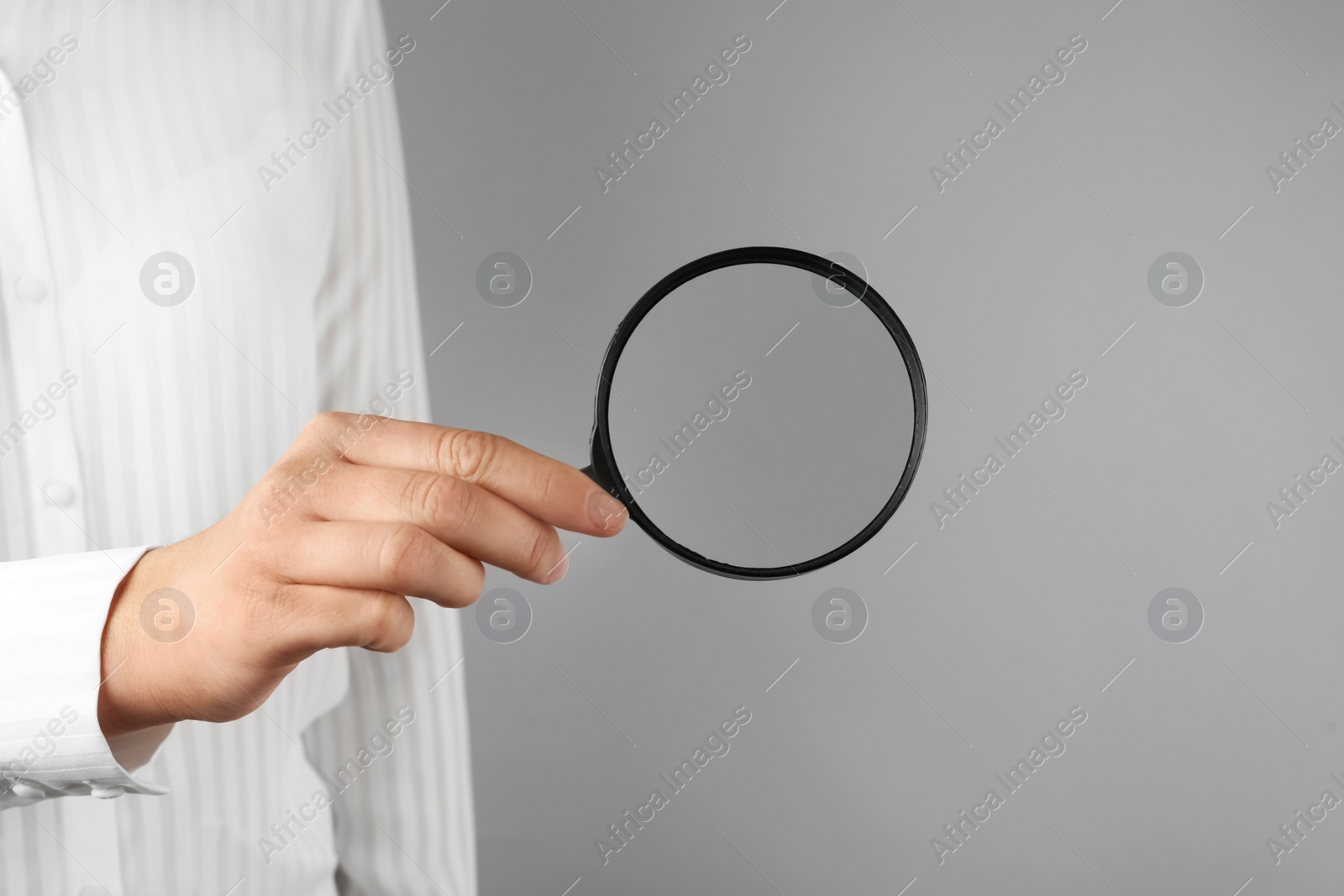 Photo of Woman holding magnifying glass on grey background, closeup. Find keywords concept
