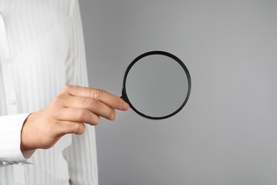 Photo of Woman holding magnifying glass on grey background, closeup. Find keywords concept