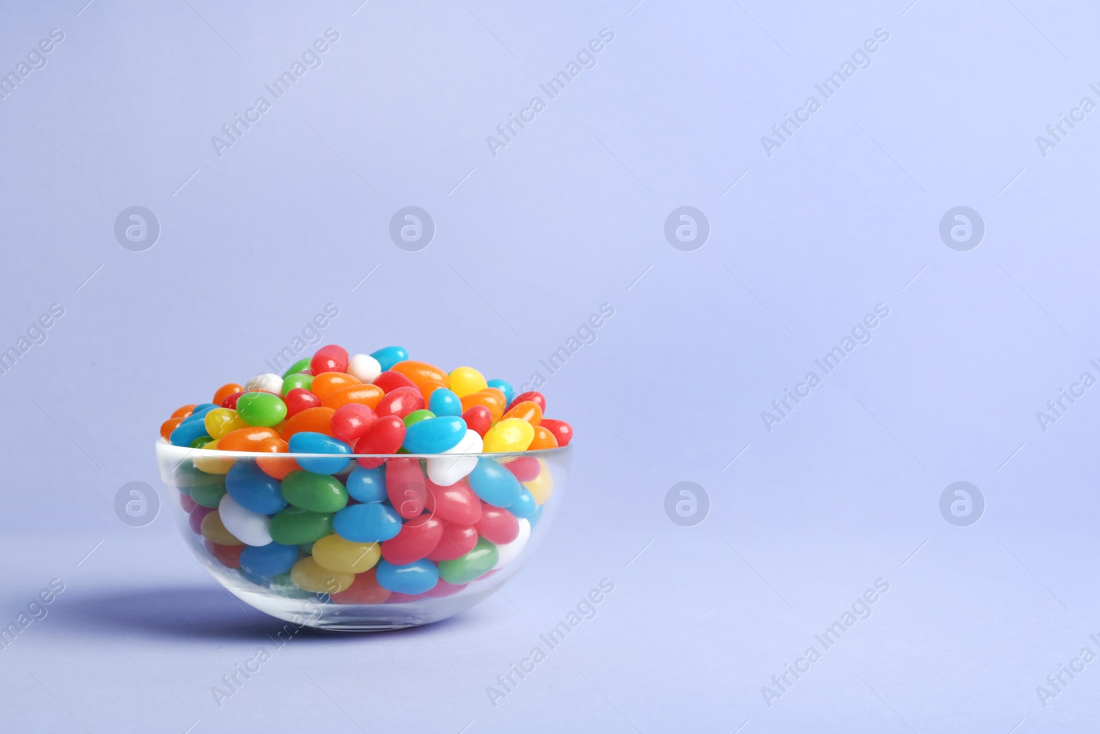 Photo of Glass bowl with delicious bright jelly beans on color background