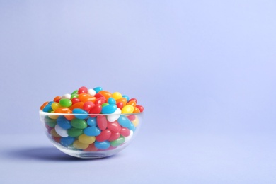 Glass bowl with delicious bright jelly beans on color background