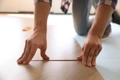 Worker installing laminated wooden floor indoors, closeup