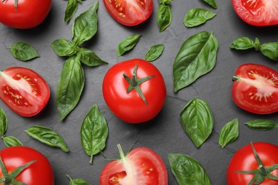 Photo of Fresh basil leaves and tomatoes on black slate table, flat lay