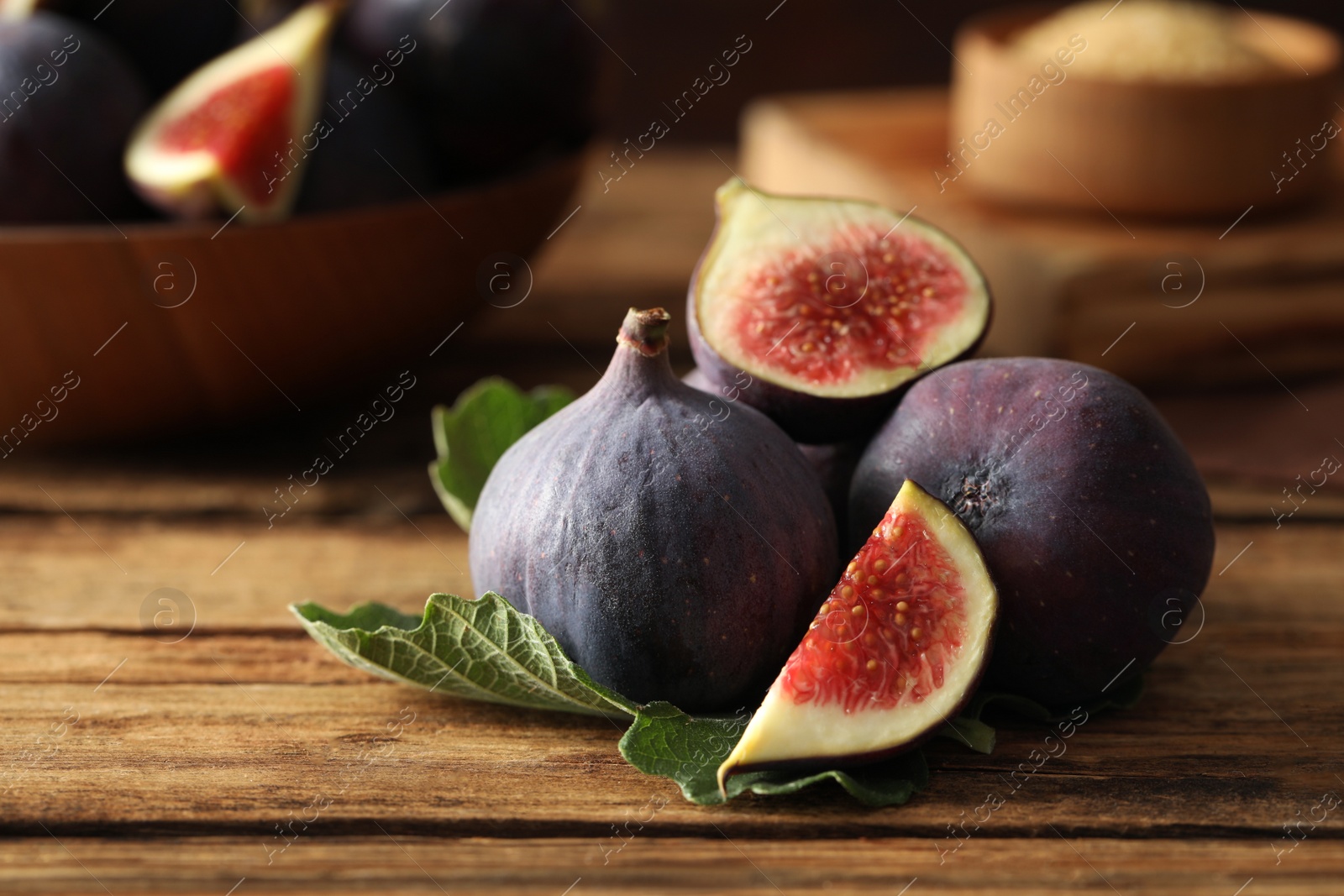 Photo of Whole and cut tasty fresh figs with green leaf on wooden table, closeup