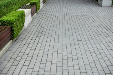 Photo of Grey sidewalk near bench and plants in park. Footpath covering